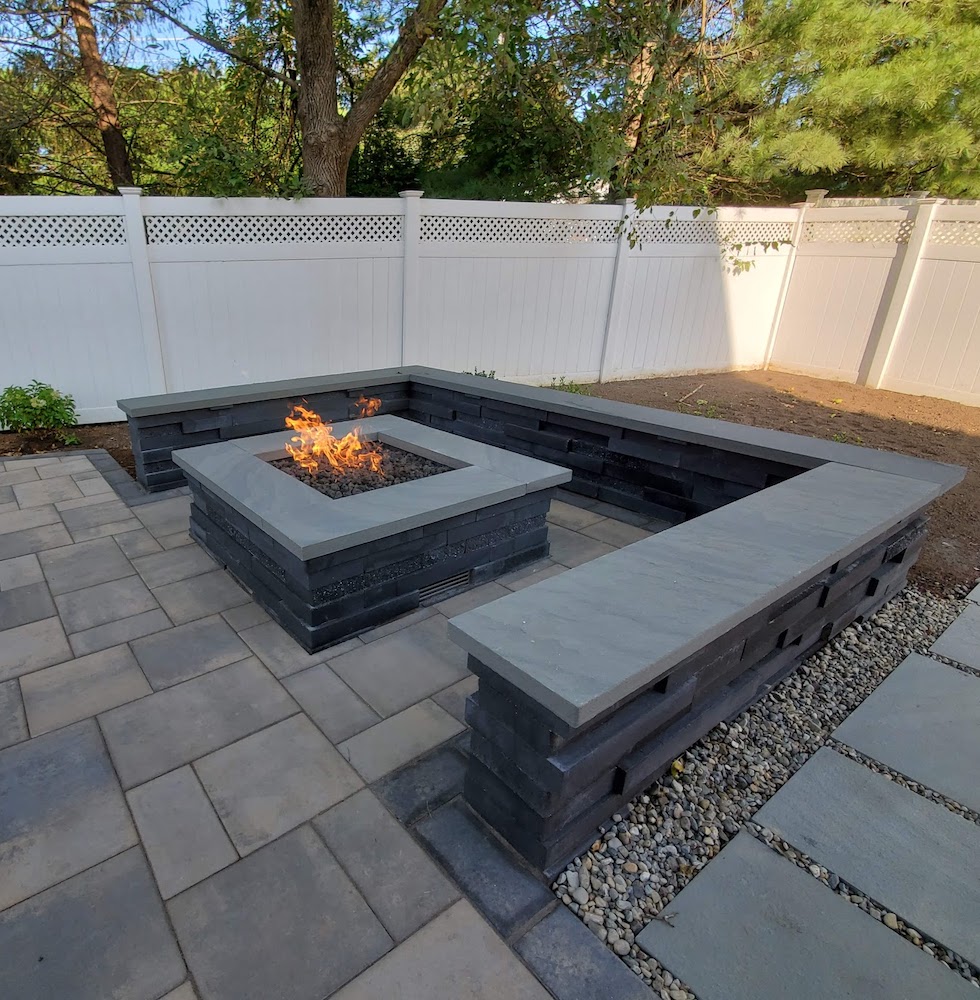 Square fire pit with fire burning and dark squared stone wall encircling the fire pit.