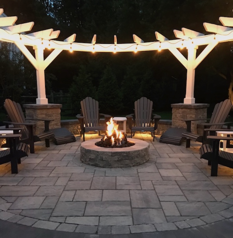 Outdoor living space with lit fire pit and lighted pergola