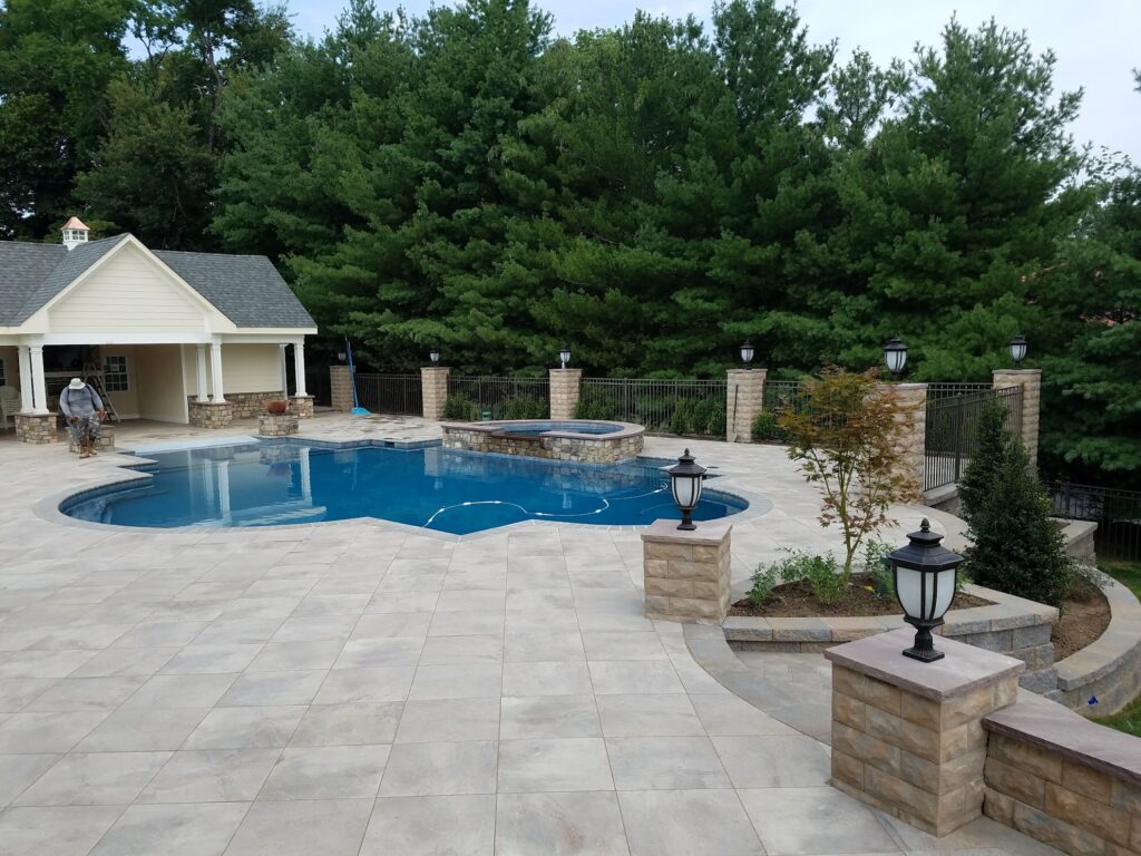 pool in the middle of a patio with steps leading down to a yard.